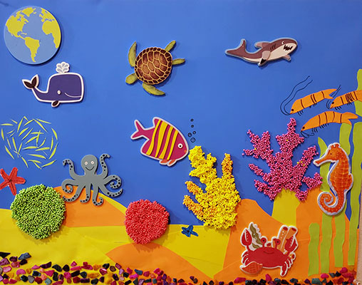 Bright paper cutouts form a coral reef. Various stickers of fish are placed in the scene.