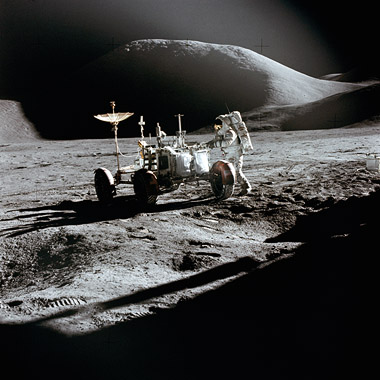 Photo of astronaut and lunar rover on the Moon, with hills in the background.
