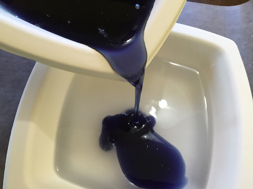 adding the purple glue mixture to the borax solution. the mixture turns into goop when they come into contact with each other