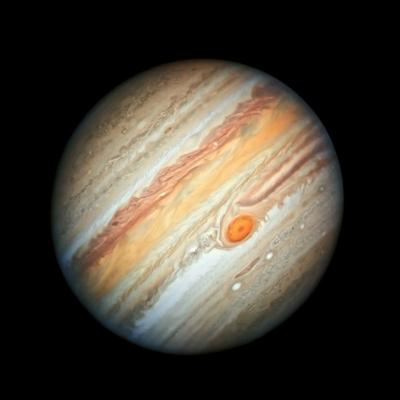 Full-disc view of colorful, banded clouds and red storm on Jupiter against a black background. The banded, swirling clouds look wispy, as if stripes of wet paint were painted and gently swirled.