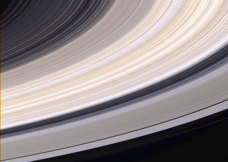 A close up view of Saturn's rings. They are grey and tan, and there are spaces in between where you can see the black color of space through them.