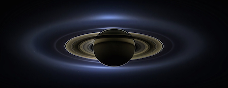A photo of Saturn where it is backlit by the sun. Saturn and its rings are nearly black, and the sun is making the edges glow.