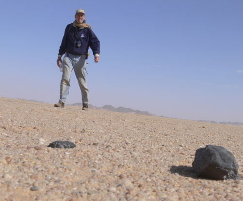 A photograph of a man walking towards a meteorite in Sudan's Nubian Desert.