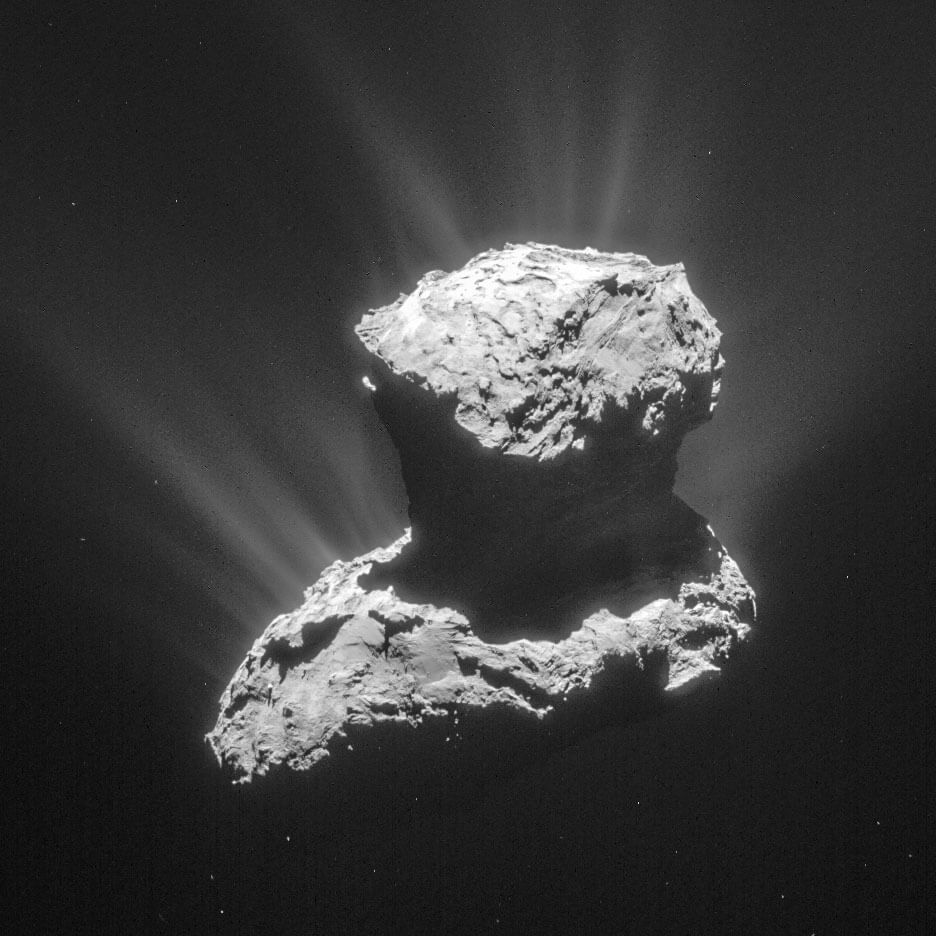 A black background with a rocky and rugged looking object illuminated from above.  The object has a larger egg-shaped part at the bottom and a smaller, rounder part at the top.  Weak jets of dust come out of the object.