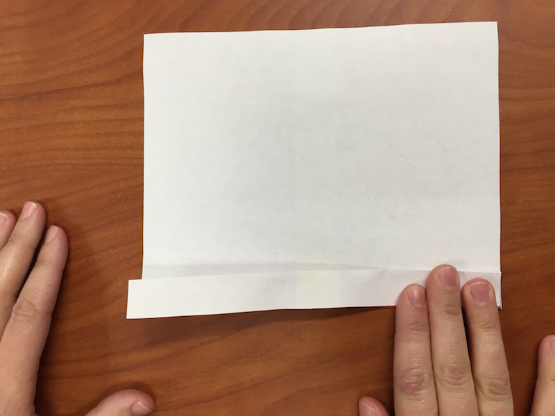 a photo of the paper turned over so the white side is facing up, and hands making the second fan fold