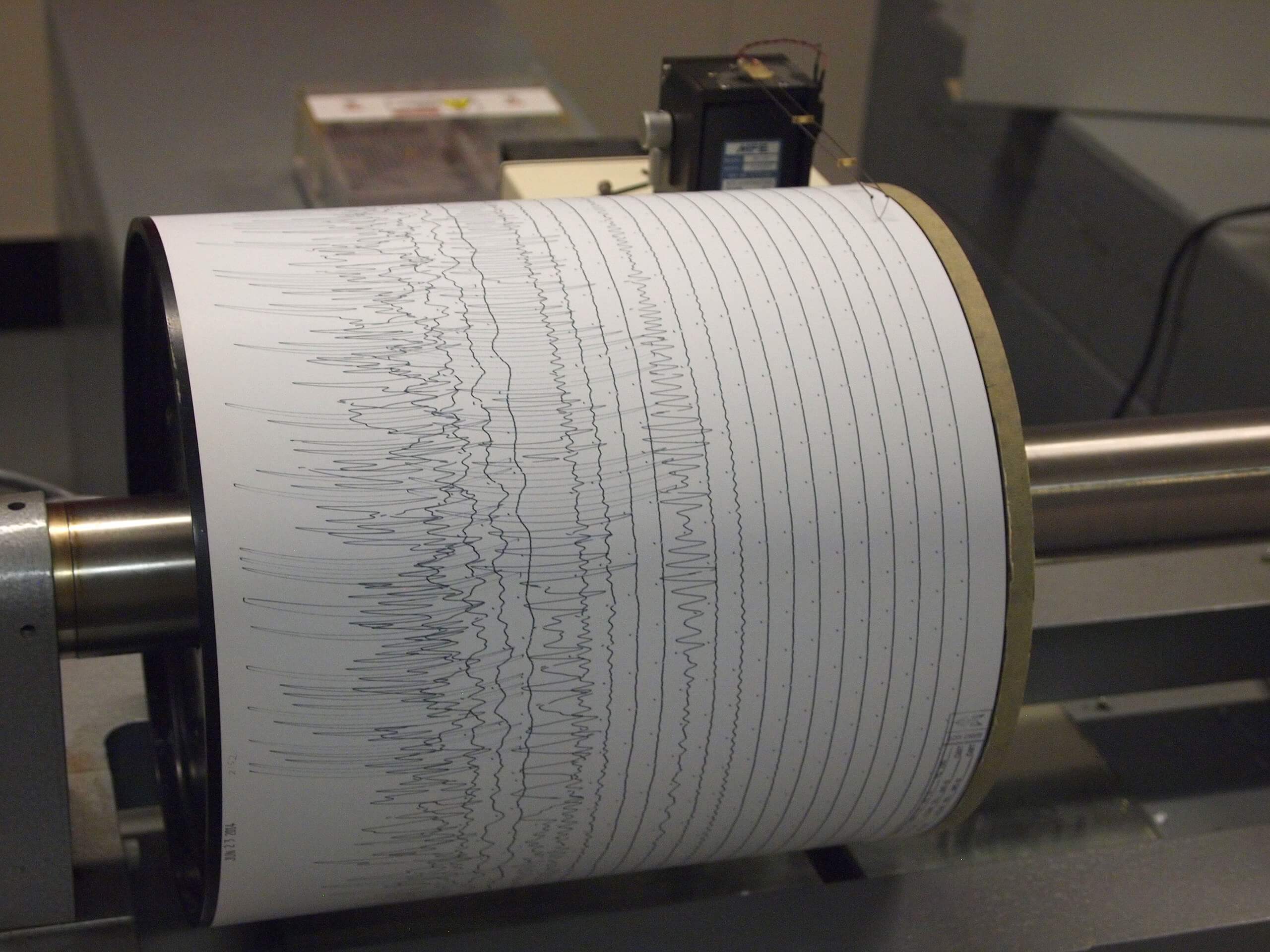 A photograph of a seismometer recording seismic waves as a series of zig-zag lines.