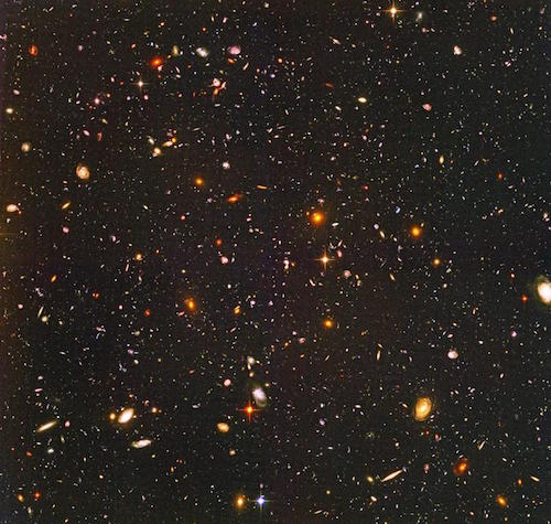 a photo taken by the Hubble Space Telescope of thousands of small galaxies of all different shapes and colors.