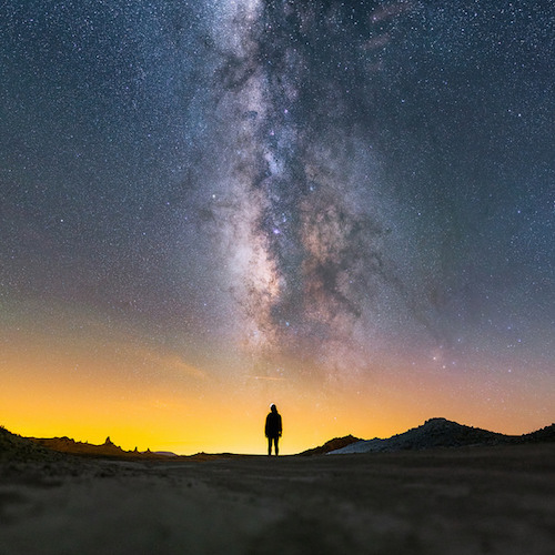 Una foto de la Vía Láctea vista desde un oscuro desierto. Los colores polvorientos iluminan el cielo.