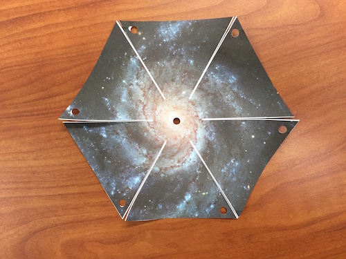 The cut out hexagonal shape of the pinwheel galaxy printout with one cut down the side along the line.