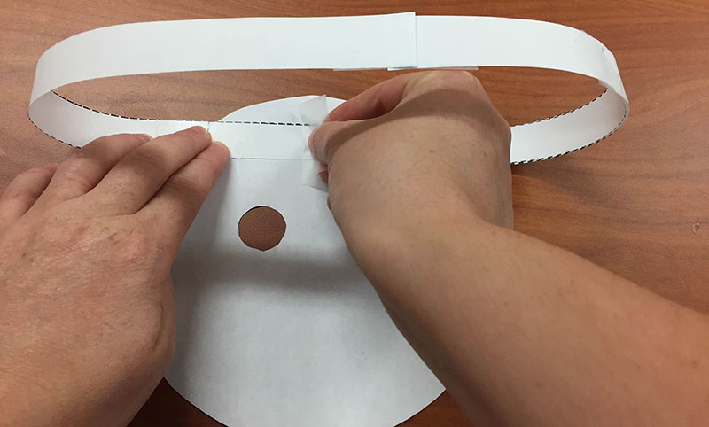 a person tapes a paper ring to the back side of a planet mask cutout