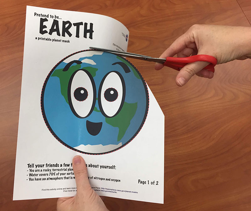 a photo of scissors cutting a cartoon of Earth out of a piece of paper