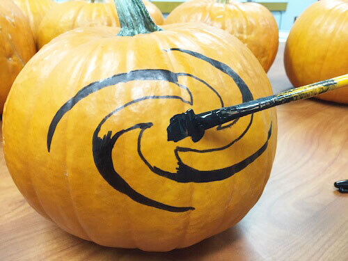 a paintbrush with black paint is being used to fill in the galaxy shape on a pumpkin