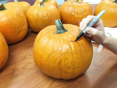 se utiliza un marcador para trazar la forma de una galaxia en una calabaza