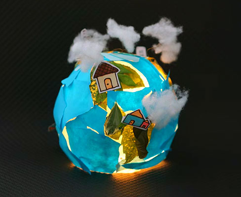 A glowing sphere covered in blue paper, leaves, paper houses and cotton balls to make it look like Earth.