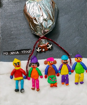 Photo of a group of clay people standing on cotton, which is meant to be snow in Antarctica. There is a foil balloon above them.