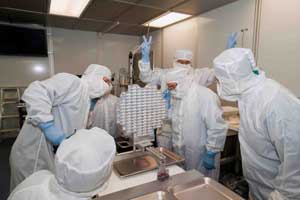 Engineers in clean room attire examine aerogel tray from Stardust capsule.