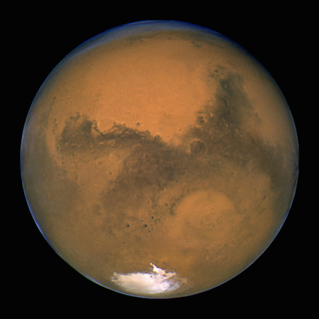 Una foto de un lado completamente iluminado de Marte, que muestra el color marrón rojizo de su superficie y una mancha blanca en el lado sur.