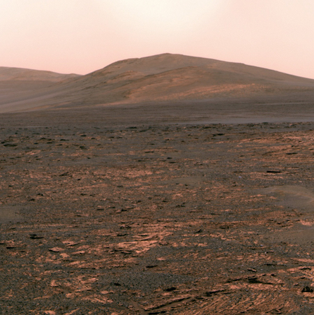 Una foto de la superficie de Marte con una colina en el fondo y muchas rocas pequeñas en primer plano.