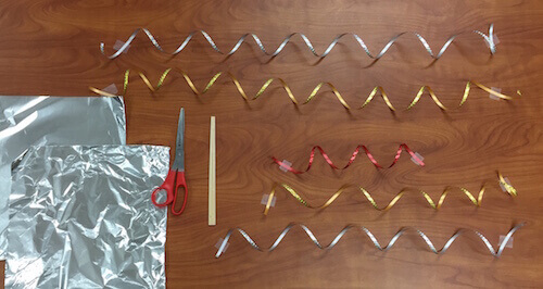 a photo of a work surface with tin foil sheets, scissors, chopsticks, and metallic ribbon piece laid out