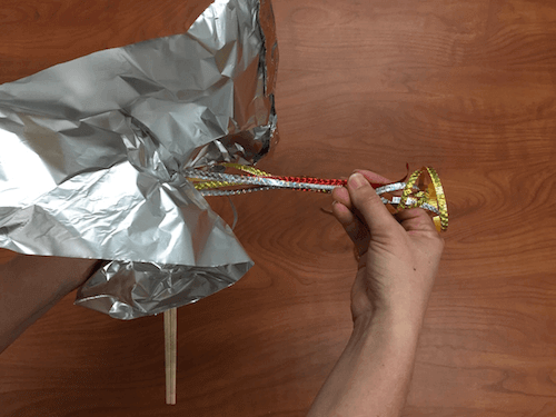a photo of the ribbon being held to one side as the tin foil sheets are gathered around the end of the chopsticks