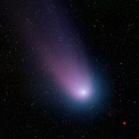 Comet NEAT nucleus is bright spot with glowing blue and violet in coma and tail trailing above and left in image.