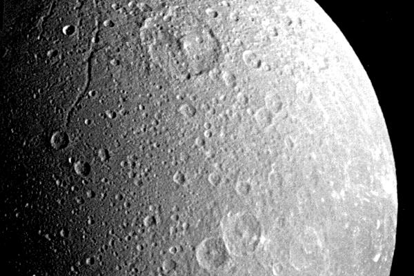 Alrededor de una cuarta parte de una brillante muestra blanco, lleno de cráteres de Dione en esta imagen.