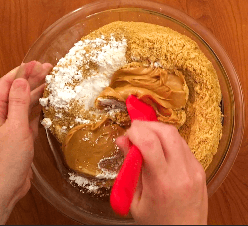 a person's hand stirs cookie ingredients with a red spatula.