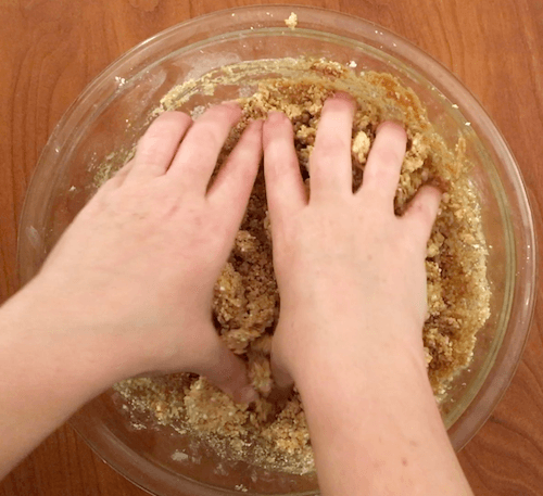 a person kneads cookie ingredients with her hands.