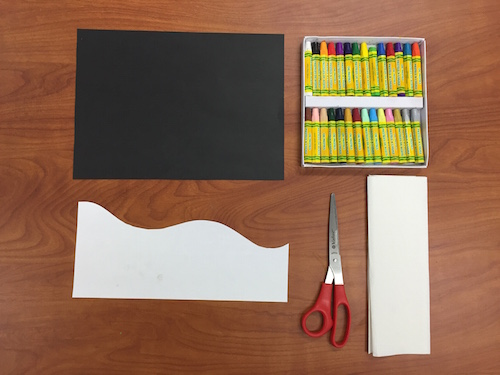 a photo of a table with a black piece of construction paper, a set of oil pastels, a piece of paper cut with a wave shape, scissors, and a paper towel.