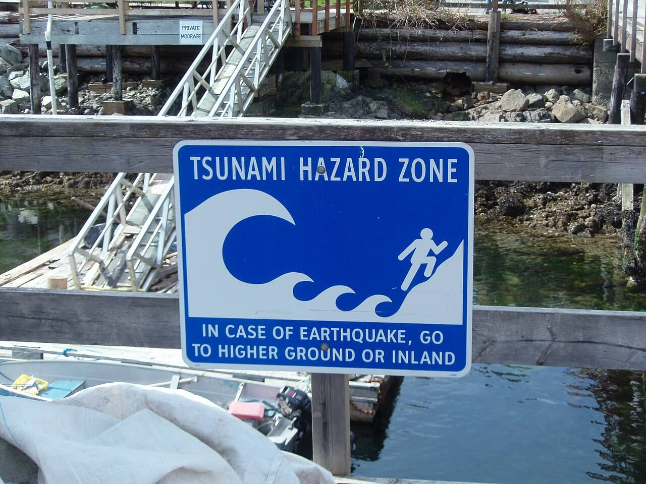 Señal de advertencia de tsunami que dice ZONA DE PELIGRO DE TSUNAMI EN CASO DE TERREMOTO VAYA A ZONAS ALTAS O TIERRA ADENTRO.