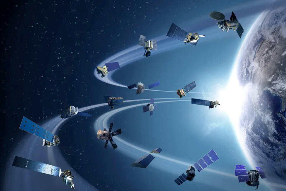 This digital illustration shows many different kinds of satellites above Earth’s surface. They are all a variety of different shapes and sizes. A portion of Earth’s horizon and surface is seen on the far right.
