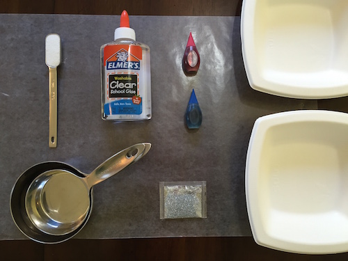 a photo of a teaspoon of borax, school glue, red and blue food coloring, glitter, measuring cups, two bowls, and wax paper on a table top