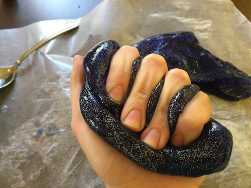a hand squeezes the universe slime to it oozes between the fingers