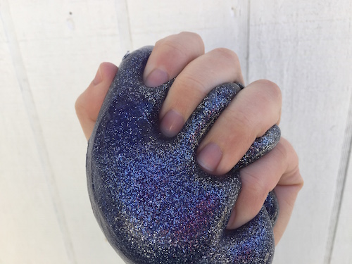 una imagen de una mano sosteniendo un limo morado universo con un mont&oacute;n de brillo